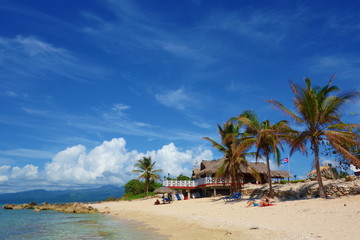 Tropical sandy beach with Cuban flag and a traditional Cuban house surrounded by palm trees, Playa Ancon, Trinidad, Cuba, Caribbean Islands