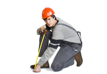 A young man in working grey clothes and orange hard helmet measuring the metric area in the room.