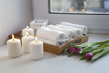 the Rolled hand towels on a tray next to the lighted candles and a bouquet of tulips in the spa salon