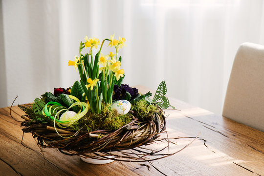 Easter table centerpiece decoration with daffodils and easter eggs arranged in a rustic wreath made of tree twigs