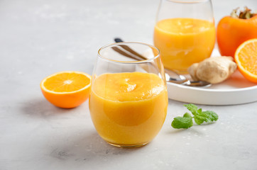 Fresh healthy smoothie with persimmon, orange and ginger on gray concrete background. Selective...