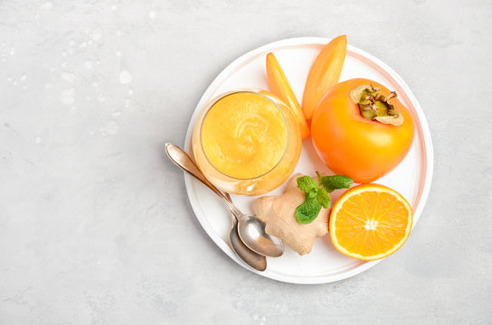 Fresh healthy smoothie with persimmon, orange and ginger on gray concrete background. Top view, flat lay, copy space.