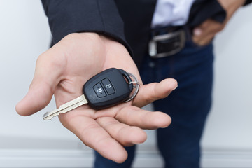 Male adult businessman in a suit  and holding a car key in his hand . White cars at the background