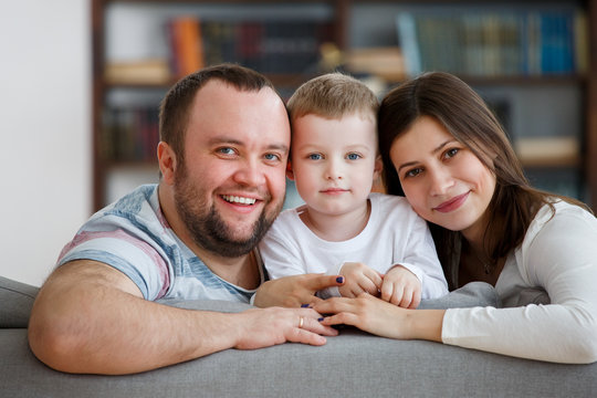 Picture of loving parents with son sitting on gray sofa