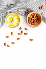 Use nut oil as cosmetics. Almond oil in jar near almond in bowl on white background top view copy space