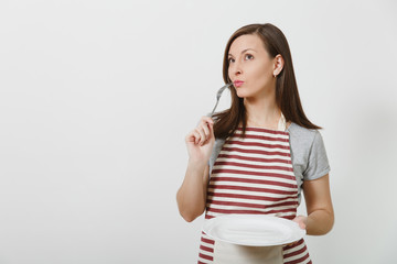 Young pretty smiling brunette caucasian housewife in striped apron gray t-shirt isolated on white background. Beautiful housekeeper woman holding white empty plate, fork. Copy space for advertisement.