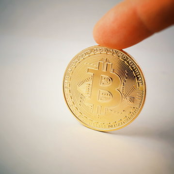 A golden bitcoin on a sheet of white paper is holding a finger. Bitcoin is a crypto currency. Bitocoin isolated on white background
