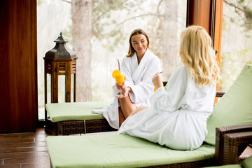 Cheerful women in bathrobes drinking juice in spa center
