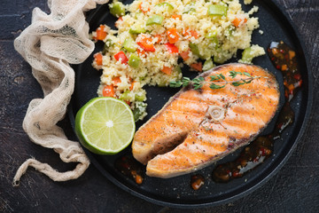 Close-up of roasted salmon fillet with cuscus, lime and sauce served on a metal tray, view from above, horizontal shot