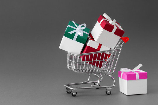 Mini shopping cart full of colorful gift boxes with ribbons. Gray background with copy space.