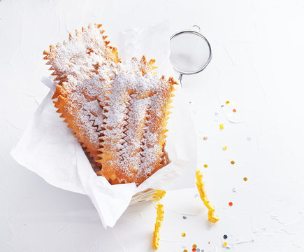 Italian Frappe or chiacchiere  - typical Italian carnival fritters dusted with powdered sugar on  white wooden table. With free text space.