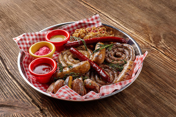Different kinds of grilled sausages with different sauces, potatoes and cabbage in plate on a wooden table.
