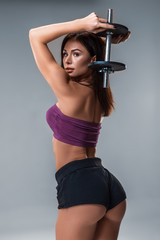 Studio portrait of a sporty young woman posing with dumbbell against a gray background. Close-up