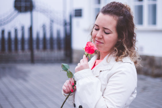 Beautiful portrait of curly woman holding red rose at the park.