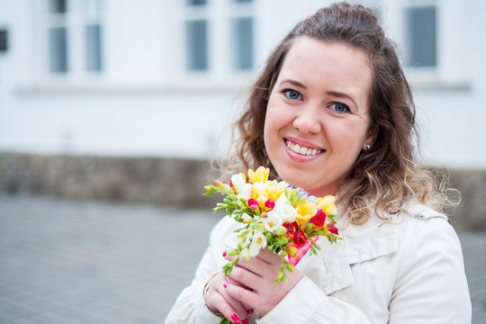 Beautiful portrait of curly woman holding flowers at the park.