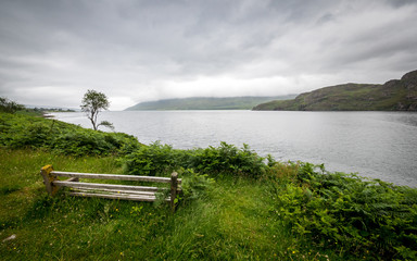 Obraz premium Loch Ewe viewpoint, Highlands, Scotland. A bench looking over the calm waters of Loch Ewe in the Scottish Highlands on a grey and overcast day.