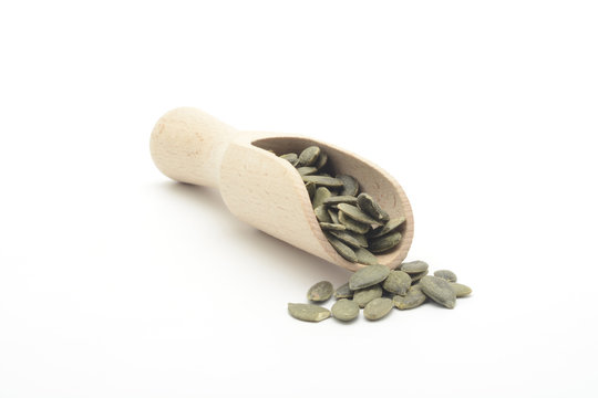 Pipas de calabaza peladas y una cuchara de madera sobre fondo blanco