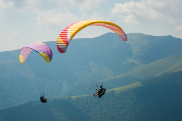 Two paragliders fly over a mountain valley on a sunny summer day. Paragliding in the Carpathians in the summer.