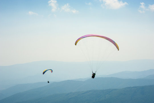 Two paragliders fly over a mountain valley on a sunny summer day. Paragliding in the Carpathians in the summer.