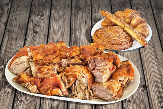 Freshly Spit Roasted Pork Shoulder Slices With Plateful Of Sesame Puff Pastry Croissant Stick And Snail Roll Set On Old Weathered Cracked Pinewood Garden Table
