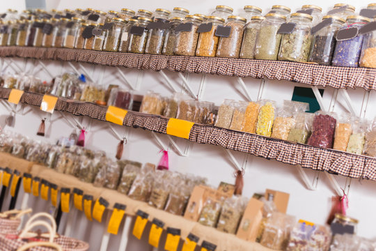 Big choice of glass cans with many different dried spices plants is standing on shelf