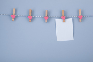 Wooden clothespin with small hearts on the blue background for the everyday notes. White sheet of paper for make a reminder