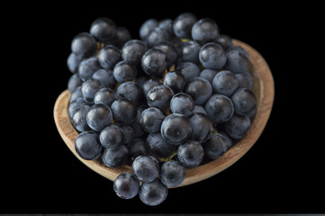 a bunch of grapes in a wooden plate on a black background. 
