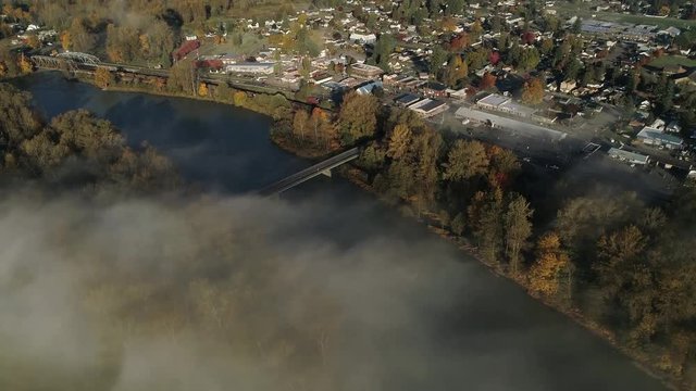Small Town by River Aerial with Train Traveling in Lowland Fog