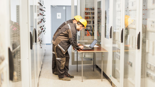Two maintenance engineers inspect relay protection system with laptop comp