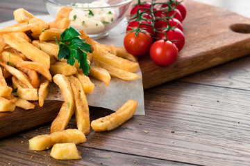 French fries, cherry tomatoes, garlic sauce on a wooden brown background, close-up. Fast food.