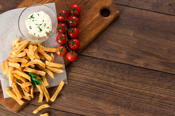 French fries, cherry tomatoes, garlic sauce on a wooden brown background, top view. Fast food.
