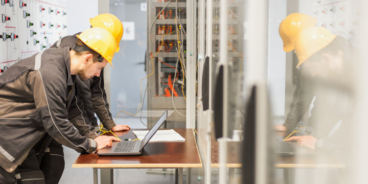 Two maintenance engineers inspect relay protection system with laptop comp