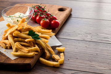 French fries, cherry tomatoes, garlic sauce on a wooden brown background, close-up. Fast food.