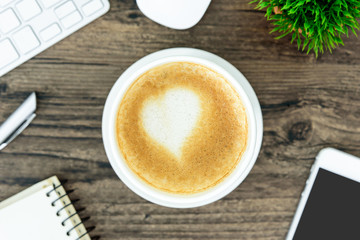 A latte coffee with art heart milk on the brown wood desk table from top view and copy space. Flat lay with desk, business and valentine concept.