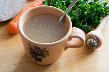 Chicken bone broth in a mug with vegetables in the background