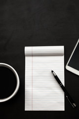 Black desk woth coffee in white cup, notebook, white smartphone and pen flat lay/ Workspace concept with black and white