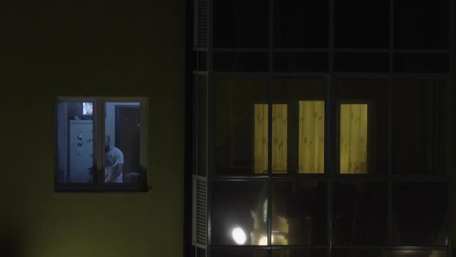 The view of the window where the man working behind the notebook. Young man working on computer at night in dark room