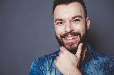 Close up portrait of Young stylish smiling guy in a denim jacket posing on a gray background.