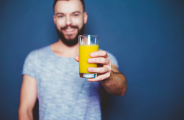 Handsome young man in a T-shirt with a glass of orange fresh juice on a gray background. Healthy...