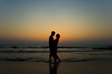 man and woman on the beach at sunset jump over the waves