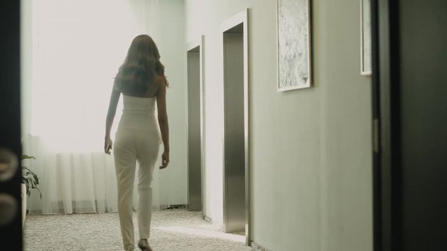 Blonde woman in white sexy suit in comes up to the elevator and presses the call button