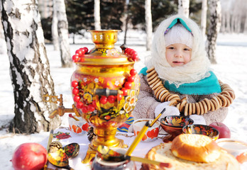 child girl in a fur coat and in a scarf in Russian style holding a large samovar in the hands of...