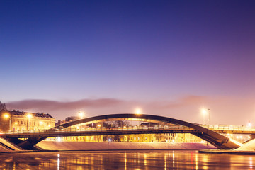 Fototapeta na wymiar Arch bridge, city lights, river, and purple clear sky during twilight blue hour in Vilnius, Lithuania