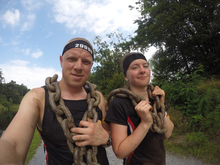 a girl with a man carries heavy chains on an extreme obstacle race and do selfie on the action camera