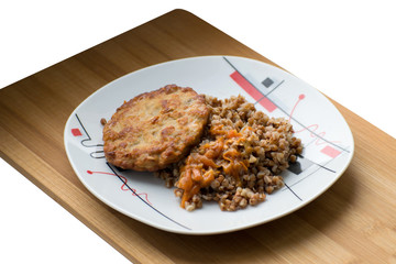 Buckwheat porridge with a cutlet on a white plate. Buckwheat cereal with schnitzel on a wooden board.