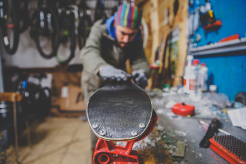 Theme repairs and maintenance of skis. The male worker is repairing work clothes, applying wax on the sliding surface onto skis mounted on ski vise of red color.The concept of service in the workshop