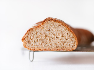 Rustic artisan French baguette home made from whole wheat and regular bread bread flour, water, yeast and sourdough fresh from the oven on cooling rack on white wooden kitchen table