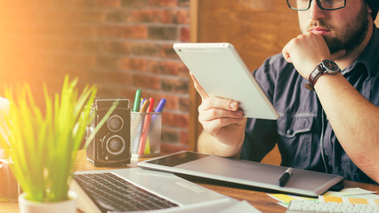 Young creative artist of web design in hat with graphic tablet in modern loft office