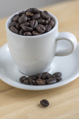 Coffee beans on white plate and in the cup on wooden background