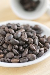 Coffee beans on white plate and in the cup on wooden background